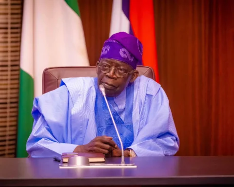President Bola Tinubu seated at a desk with a microphone in front of Nigerian flags