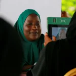 A woman in a green hijab is photographed on a green tablet at a voter registration desk