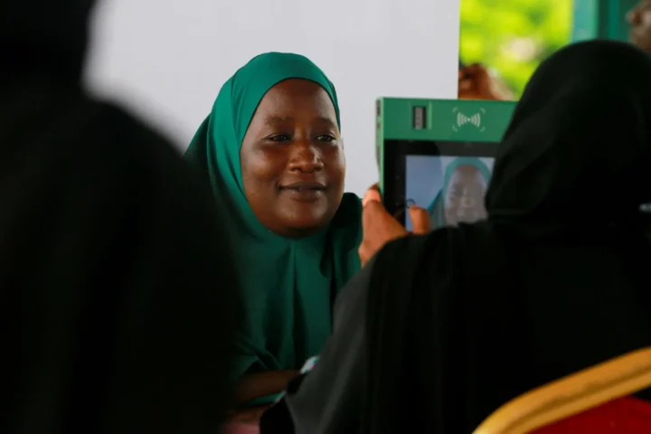 A woman in a green hijab is photographed on a green tablet at a voter registration desk
