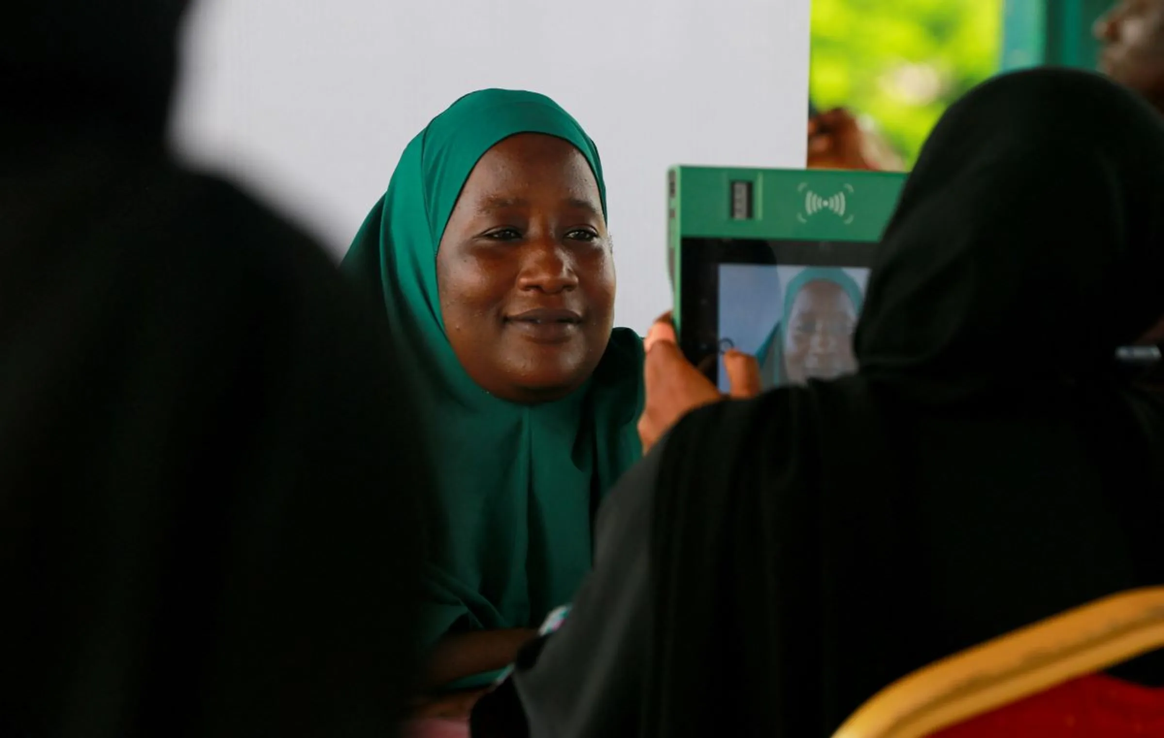 A woman in a green hijab is photographed on a green tablet at a voter registration desk