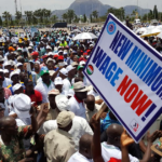 Workers at a Nigeria Labour Congress rally in Abuja holding a sign that reads New Minimum Wage Now