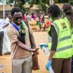 Health workers in Ministry of Health vests spray hand sanitiser on a man’s hands at a screening point in Kenya