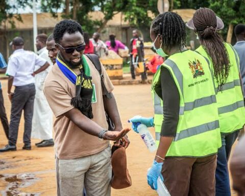 Health workers in Ministry of Health vests spray hand sanitiser on a man’s hands at a screening point in Kenya