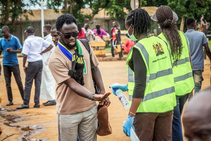 Health workers in Ministry of Health vests spray hand sanitiser on a man’s hands at a screening point in Kenya
