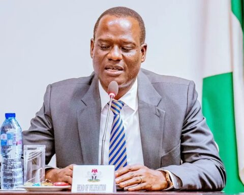 A Nigerian government official speaking at a table with a Head of Delegation name card and the Nigerian flag behind him