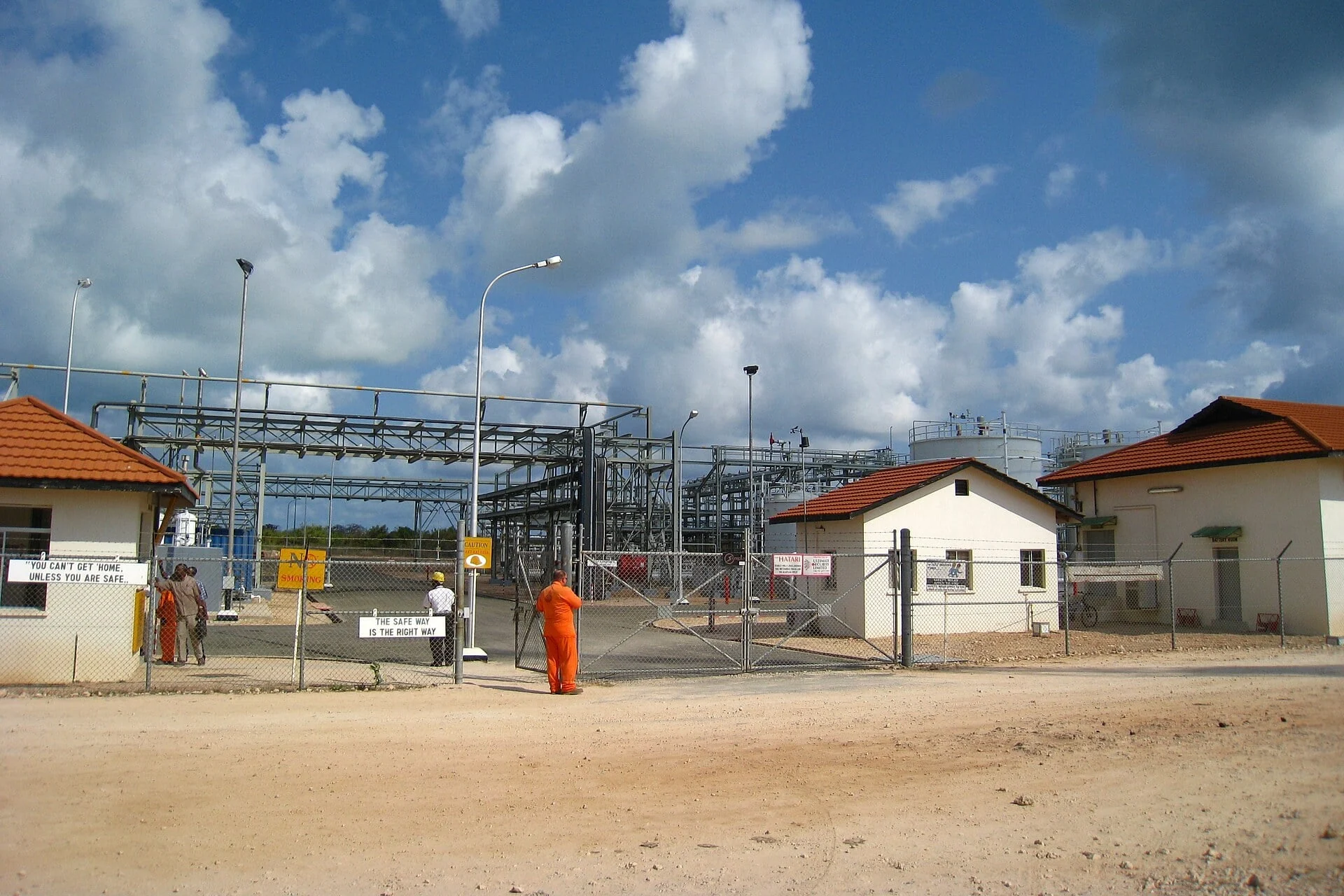 Gas processing plant at Mnazi Bay in southern Tanzania with pipework behind a fenced gate and a worker in orange overalls