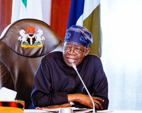 President Bola Tinubu speaking at a desk with the presidential seal on the chair behind him