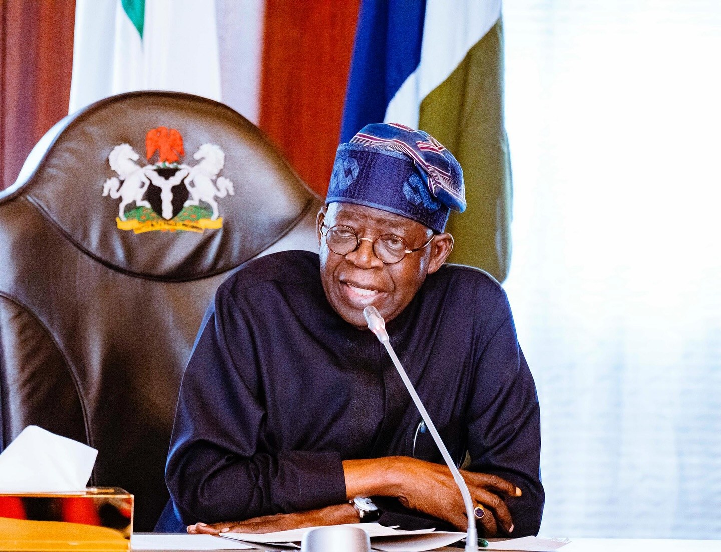 President Bola Tinubu speaking at a desk with the presidential seal on the chair behind him