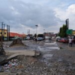 A flooded, broken road in Lagos with potholes, piled-up rubbish and cars parked along the side